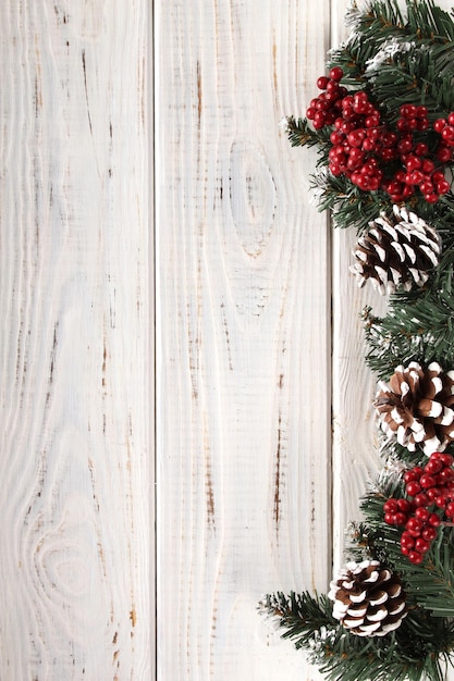 Fond de Noël. Planches de bois blanches avec branches de sapin, pommes de pin, neige et baies rouges