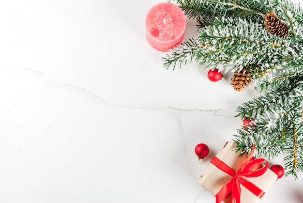 Fond de Noël pour carte de voeux. Branches d'arbres de Noël avec effet neige avec ruban rouge festif, pommes de pin, coffrets cadeaux et bougies, sur fond de marbre blanc vue de dessus