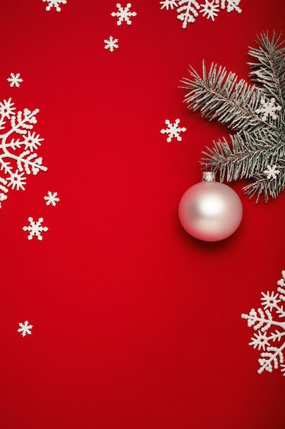 Fond de Noël avec sapin, boule blanche et flocons de neige sur rouge.