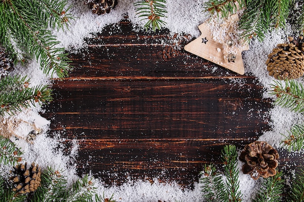 Fond de Noël, sapins et cônes sur une table en bois, écrasée par la neige blanche, espace copie, vue de dessus.