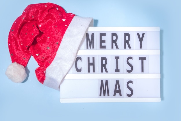 Fond de Noël simple avec bonnet de Noel et Lightbox avec texte Joyeux Noël, vue de dessus flatlay fond bleu clair