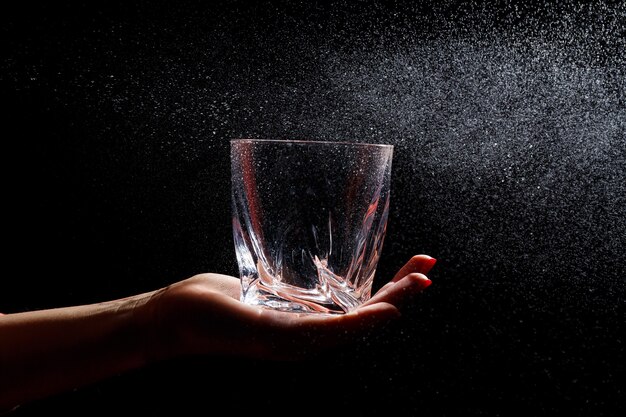 Le fond noir dessus est un gros plan d'un verre propre dans une main. Vaporiser sur un verre d'eau. Verre isolant