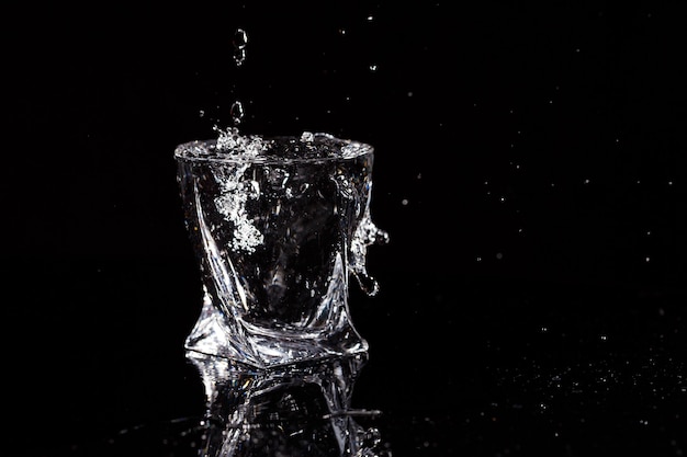 Le fond noir est un verre dans lequel tombe une goutte d'eau. Éclaboussures d'eau sur le verre