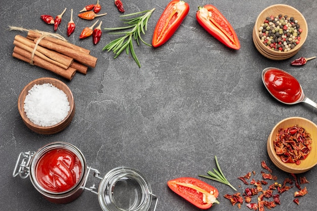 Fond de nourriture. Bâtonnets de cannelle. Pois de senteur, poivrons rouges dans des bols. Poivrons rouges crus et brins de romarin. Sauce tomate en pot. Mise à plat. Fond noir. Espace de copie.