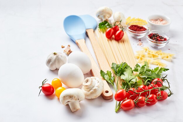 Fond de nourriture avec place pour le texte, avec différents types de pâtes, tomates, herbes, champignons, œufs, assaisonnements dispersés sur fond de marbre clair. Concept de cuisine italienne