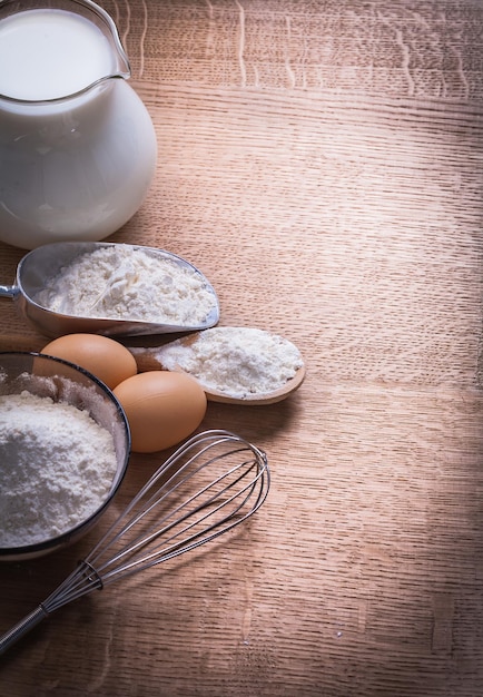 Fond organisé de farine dans un bol de cuillère et d'oeufs scoop pichet de corolle avec du lait sur une planche de bois nourriture et boisson nature morte