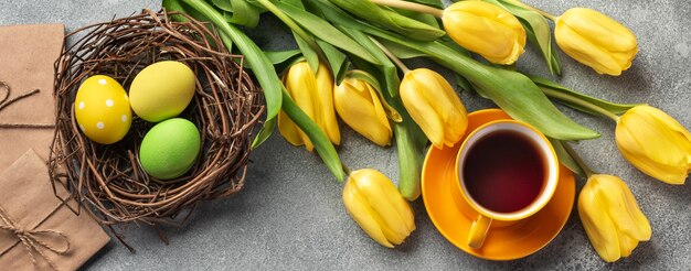 Fond de Pâques avec des œufs bleus et verts et une tasse de thé dans un nid et des tulipes jaunes. Vue de dessus avec espace de copie.