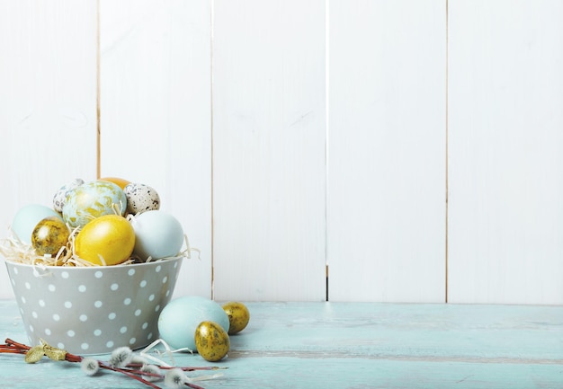 Fond de Pâques avec des oeufs de Pâques bleus et or devant un mur en bois blanc avec un espace réservé au texte