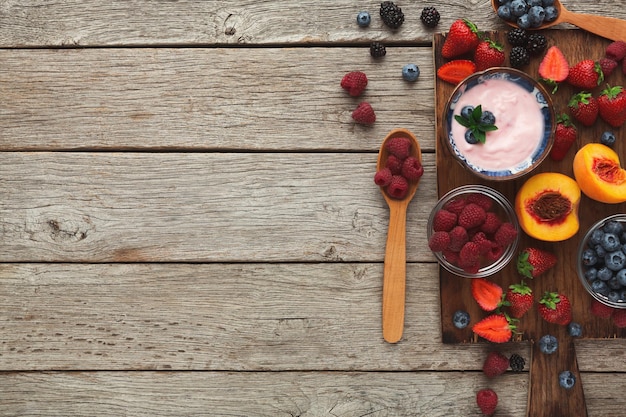 Fond de petit déjeuner délicieux. Yaourt grec léger et baies fraîches bio sucrées pour les repas du matin sur une table en bois rustique avec espace de copie. Vue de dessus sur une alimentation quotidienne riche