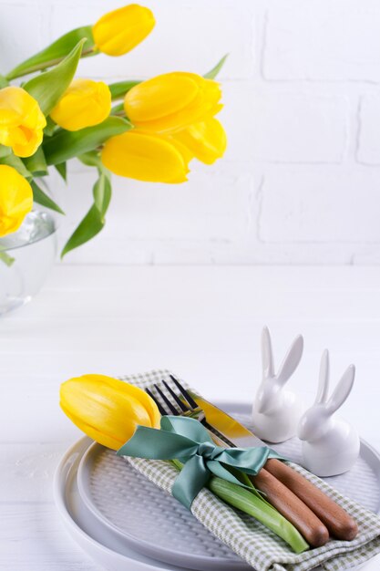 Fond de printemps de Pâques pour le menu. Décoration d'oeufs de Pâques, lapin, serviette en lin sur assiette et couverts de cuisine sur table en bois blanc.