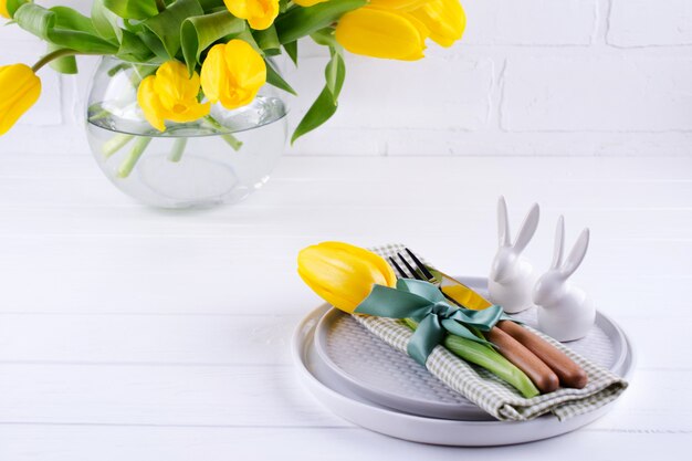 Fond de printemps de Pâques pour le menu. Décoration d'oeufs de Pâques, lapin, serviette en lin sur assiette et couverts de cuisine sur table en bois blanc.