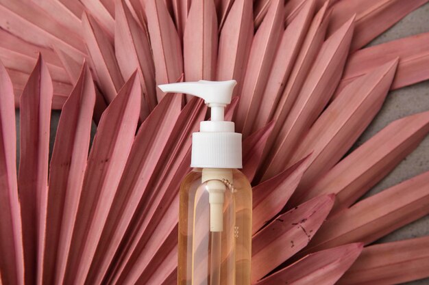 Fond de produit de beauté naturel avec une bouteille et des feuilles de palmier roses séchées