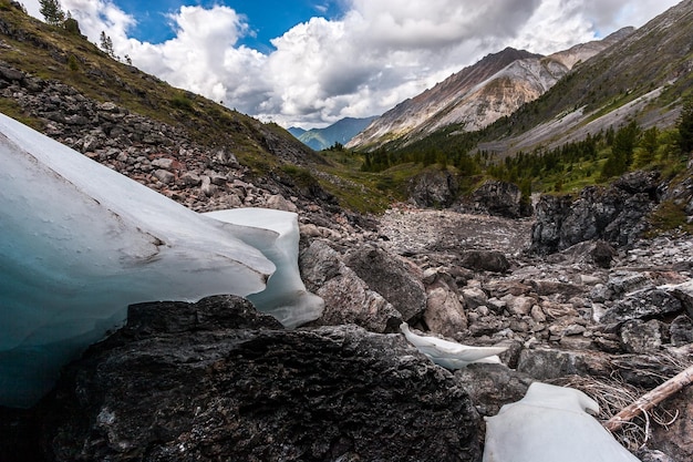 Le fond rocheux du ruisseau et les restes de glace sur les pierres Des chaînes de montagnes avec des pentes vertes au loin Ciel bleu avec des nuages Horizontal