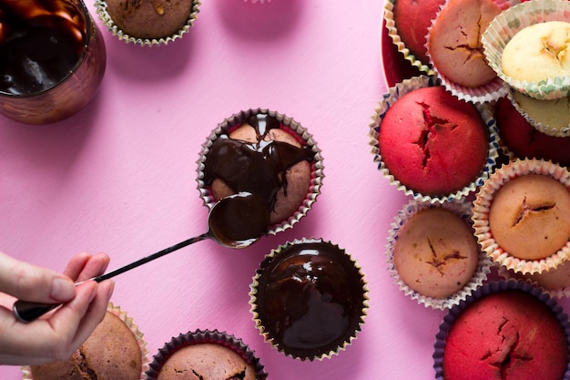 Sur fond rose, une femme décore des cupcakes avec du chocolat et des baies. muffins maison dans la cuisine