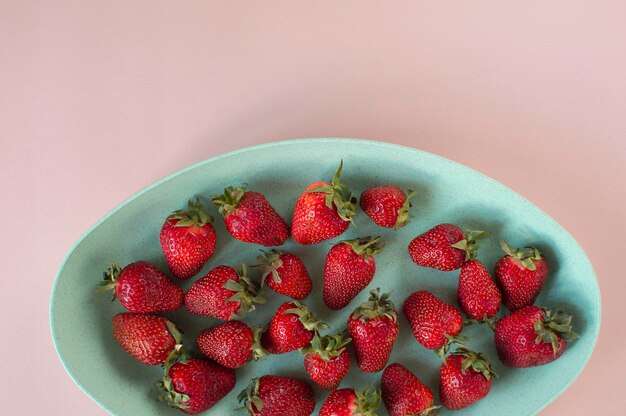 Sur fond rose, il y a une éco-tasse verte avec des fraises fraises bio juteuses rouges Fraises rouge vif en gros plan