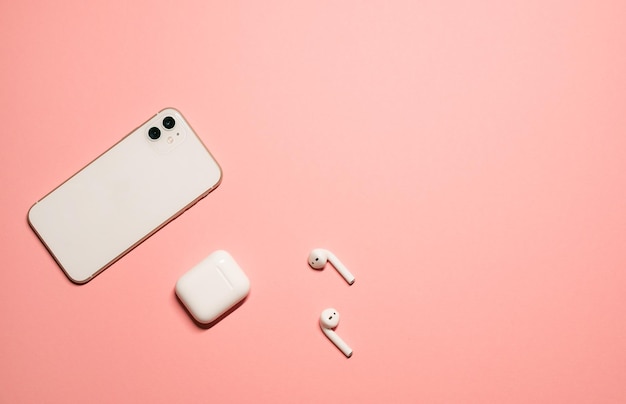 fond rose pastel avec un smartphone blanc et des écouteurs sans fil avec un étui de chargement