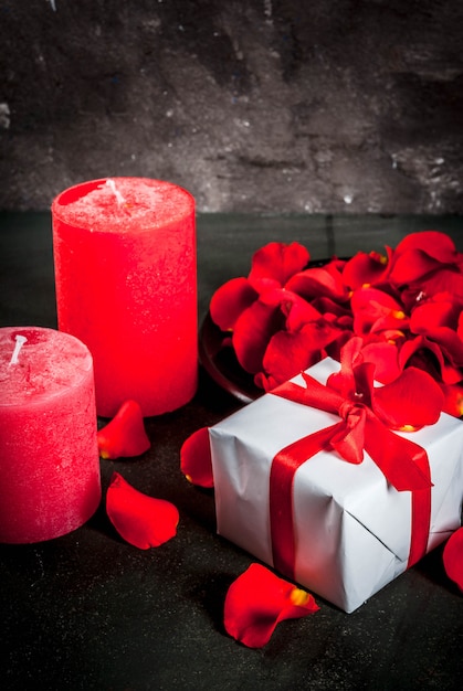 Photo fond de saint valentin avec des pétales de fleurs roses, coffret cadeau enveloppé blanc avec ruban rouge et bougie rouge de vacances, sur fond de pierre sombre, espace copie