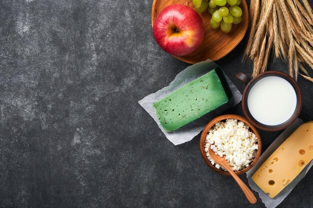 Fond de Shavuot heureux pour la célébration juive religieuse traditionnelle de Shavuot Lait et fromage blé et fruits mûrs Produits laitiers sur fond gris foncé Concept de Shavuot Vue de dessus Maquette