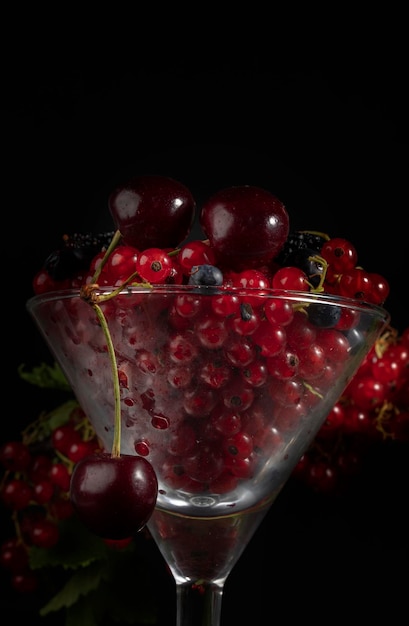 Sur un fond sombre dans un gobelet en verre se trouvent des baies rouges de cerises et de groseilles