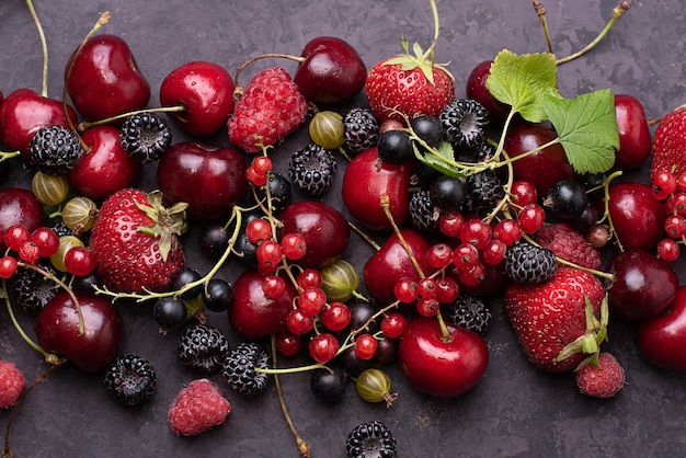 Fond sombre avec des fraises de baies d'été éparses, groseilles, framboises, cerises, gros plan.