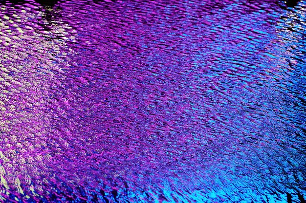 Fond de surface de l'eau. Petite ondulation à la surface de l'eau éclairée par une lumière de couleur différente. Vagues abstraites sur la surface de l'eau sombre. Faible profondeur de champ.