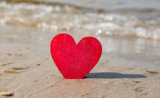 Fond tropical pour la Saint-Valentin Le coeur en bois rouge est situé sur la plage de sable Derrière la mer ou l'océan Amour pour les voyages