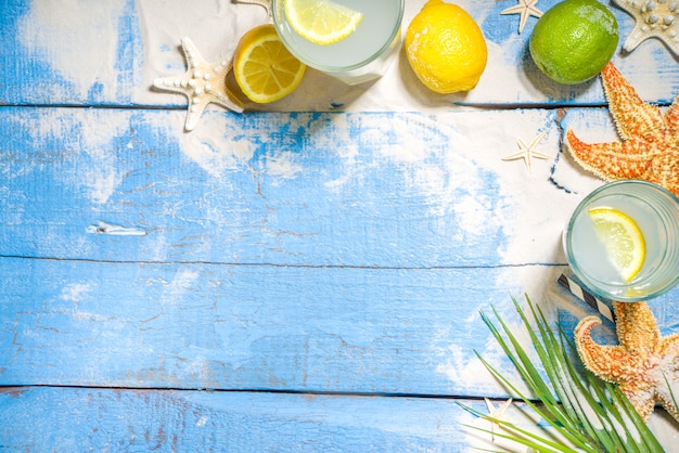 Fond tropical de vacances de vacances d'été avec des boissons de limonade. Cocktail Mojito avec des ombres claires et sombres, sur un fond tropical avec des étoiles de mer, des feuilles de palmier copient l'espace pour le texte