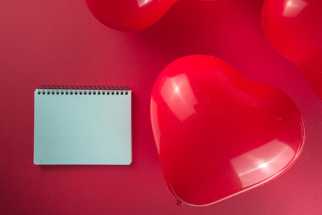 Fond de vacances douce Saint-Valentin avec des ballons en forme de coeur rouge sur fond rouge, avec bloc-notes, tablette, espace de copie de cadre de vue de dessus flatlay, maquette pour la carte de voeux de la Saint-Valentin