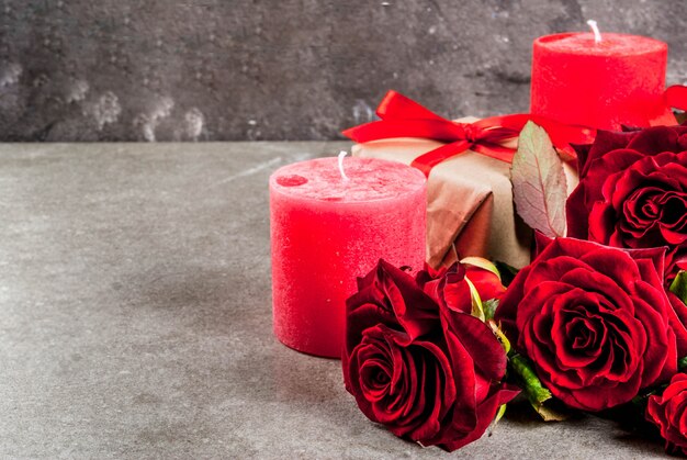 Fond de vacances, Saint Valentin. Bouquet de roses rouges, cravate avec un ruban rouge, avec coffret cadeau enveloppé et bougie rouge