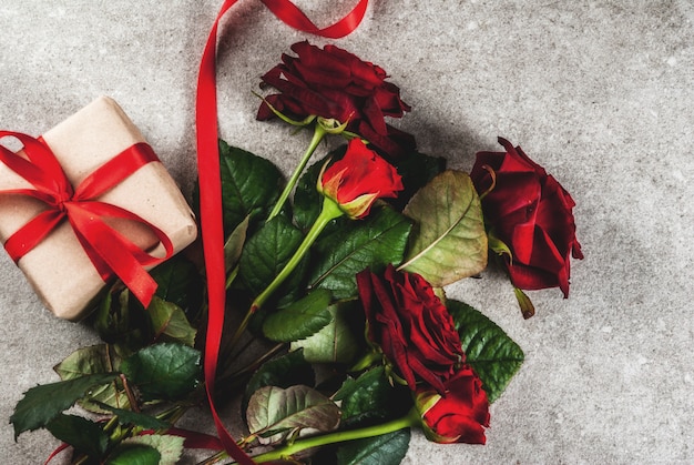 Fond de vacances, Saint Valentin. Bouquet de roses rouges, cravate avec un ruban rouge, avec coffret cadeau enveloppé et bougie rouge