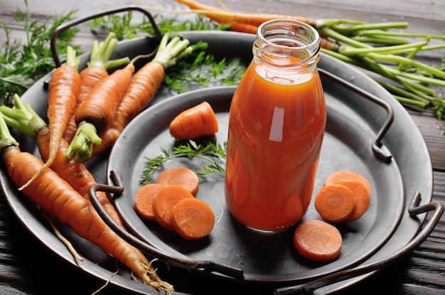 Fond végétarien de vieux plateau avec carottes et petite bouteille de jus sur ardoise