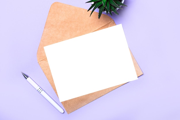 Sur un fond violet, il y a un stylo blanc, une plante en pot, une enveloppe artisanale et une carte vierge blanche avec un endroit pour insérer du texte Modèle de vue de dessus