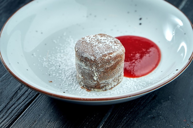 Fondant au chocolat dessert avec sauce aux baies et sucre en poudre dans une assiette blanche sur table en bois