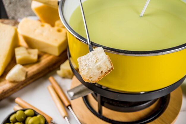 Fondue suisse gastronomique dans un plat à fondue traditionnel, avec fourchettes, divers fromages, olives, pain et raisin