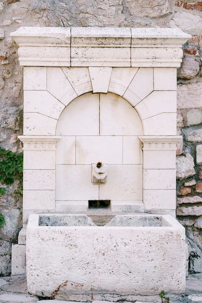 Une fontaine carrelée avec un bol en pierre dans un mur pavé.