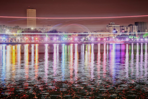 Fontaine éclairée dans le lac contre l'arc-en-ciel dans la ville la nuit