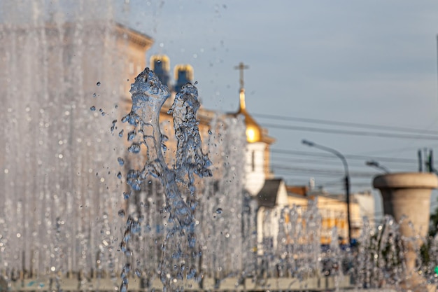 Fontaine de la ville avec des éclaboussures et des jets d'eau sur fond de bâtiments et un dôme d'église de couleur dorée avec une croix sous un ciel bleu par une claire journée d'été