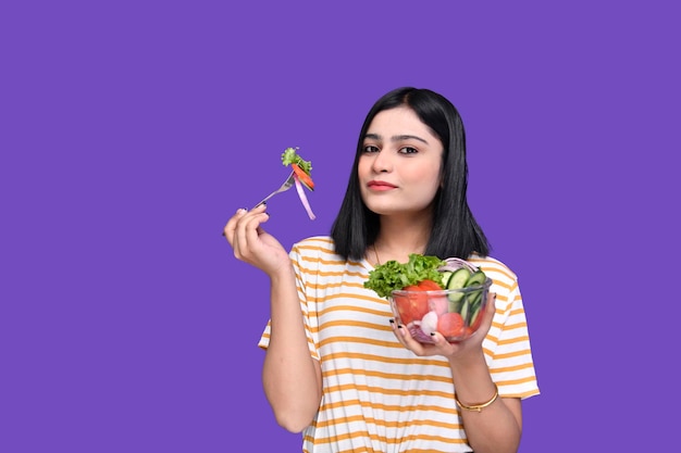 Foodie girl holding cuillère et bol de salade posant sur fond violet modèle pakistanais indien
