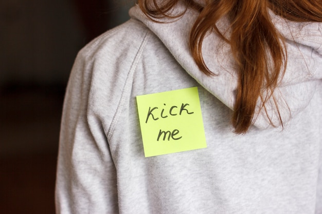 Fool&#39;day jok. Autocollant &quot;Kick me&quot; sur le dos d&#39;une adolescente.