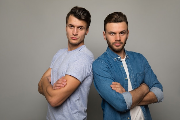 La force des frères. Deux jeunes hommes en tenue décontractée se tiennent dos à dos avec des expressions faciales joyeuses, posant les bras croisés et souriant à la caméra.