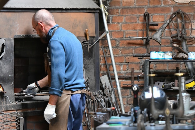 Un forgeron expérimenté travaille à feu ouvert. Un forgeron éteint une flamme dans une forge avec un feu d'artifice d'étincelle, forge du fer chaud dans un atelier