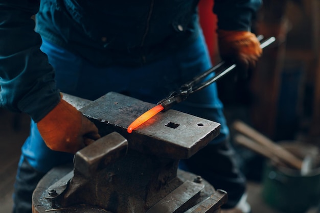 Le forgeron forge et fabrique des détails métalliques avec un marteau et une enclume à la forge
