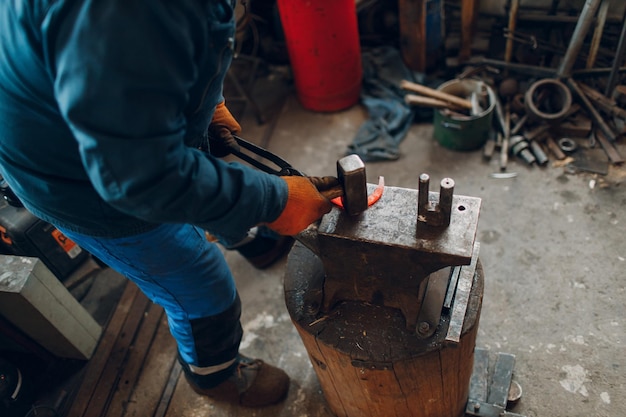 Le forgeron forge et fabrique des détails métalliques avec un marteau et une enclume à la forge