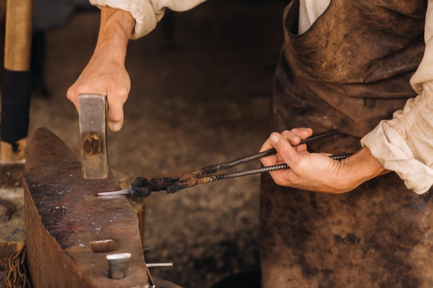 Un forgeron forge manuellement du métal rouge sur une enclume avec un marteau
