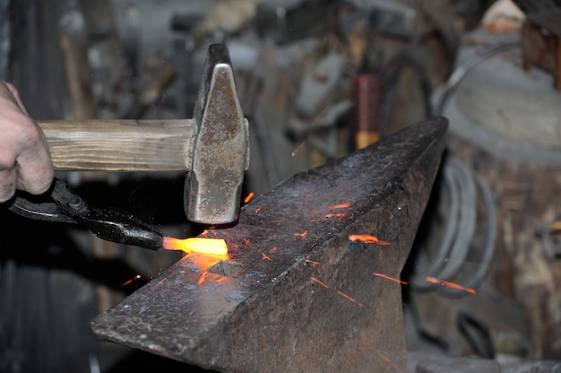 Forgeron travaillant le métal avec un marteau sur l'enclume dans la forge