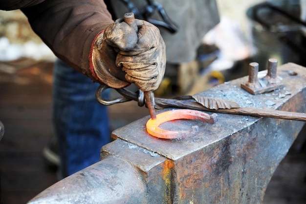 Forgeron travaillant le métal avec un marteau sur l'enclume dans la forge