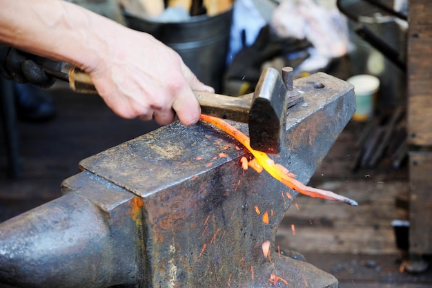 Forgeron travaillant le métal avec un marteau sur l'enclume dans la forge