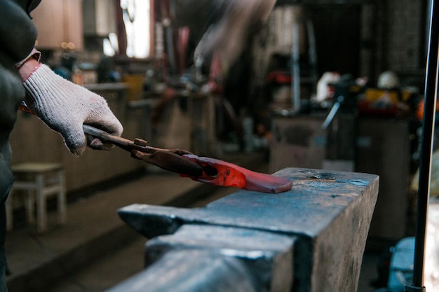 Forgeron travaillant avec une pièce en métal rouge chaud de nouvelle hache sur l'enclume à la forge se concentrer sur les mains