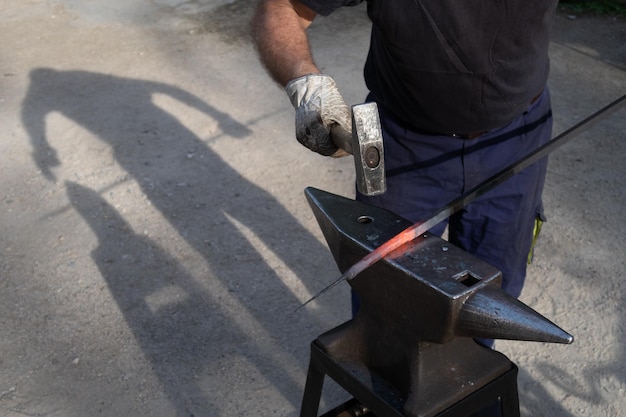 Photo un forgeron travaille la forge avec un marteau sur l'enclume