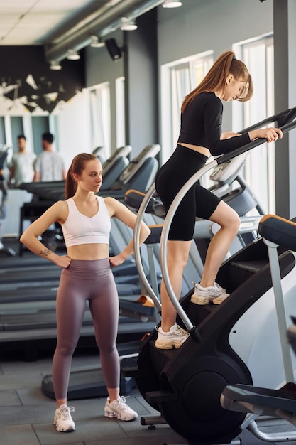 Formateur aidant à diriger l'hippodrome Deux femmes en vêtements de sport ont ensemble une journée de remise en forme dans la salle de sport